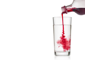 Cranberry syrup pouring into water glass on white background