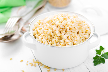Bulgur wheat. Boiled bulgur cereal in pot on white kitchen table. Healthy vegetarian food