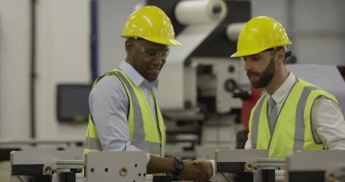 A manager and his foreman shake hands in a production factory. In slow motion
