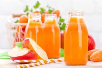 Fresh carrot and apple juice on white background. Carrot and apple juice in glass bottles on white table, closeup