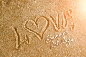The word love is painted on the sand and the inscription is summer holidays. Beach background. View from above. The concept of summer, summer kanikkuly, vacation, holydays.
