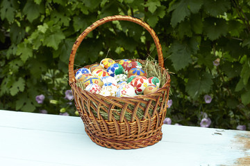 Fototapeta na wymiar Wicker basket with Easter eggs against the background of summer flowers
