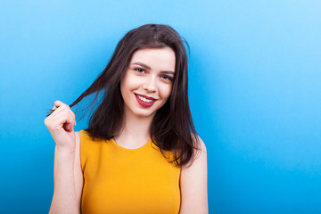 Fototapeta premium Smilng woman playing with her hair on blue background