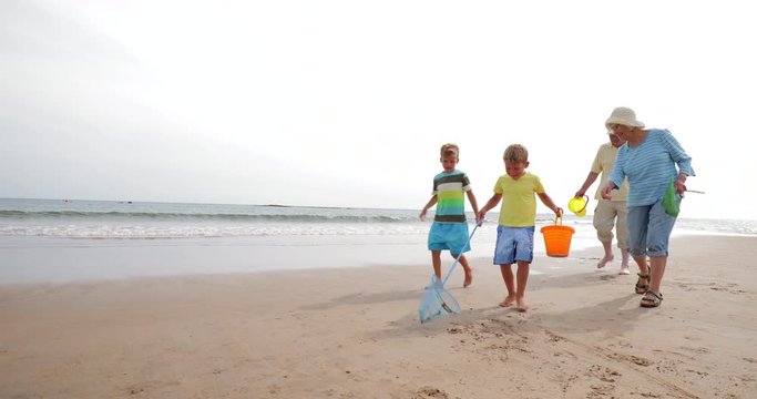 Slow motion shot of two brothers and their grandparents searching for shells on the beach.