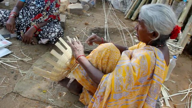 Indian elder lady on yellow saree sitting on the ground making bamboo baskets on the street in Mysore, Karnataka, India. Hard work, humble, poor old rural village woman blue collar job concept