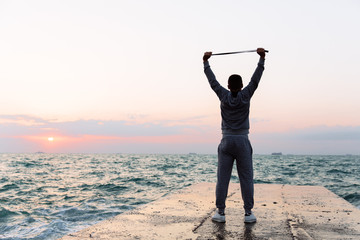 Fototapeta premium Full length view of sportsman stretching with jump rope, on pier