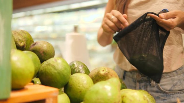 Young Mixed Race Woman Shopping without Plastic Bags in Grocery Store. Vegan Zero Waste Girl Choosing Fresh Avocados in Supermarket. 4K.