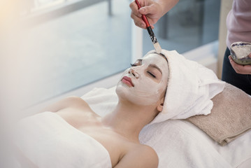 Obraz na płótnie Canvas Masseur doing cream mask on face of beautiful young woman relaxing in the spa salon.