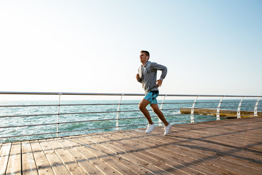 Side View Of Athletic Guy Running On Quay, Near The Sea