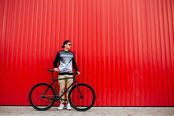 Stylish man standing with bike against the urban red wall