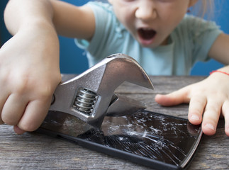 evil little girl breaks a smartphone with a wrench