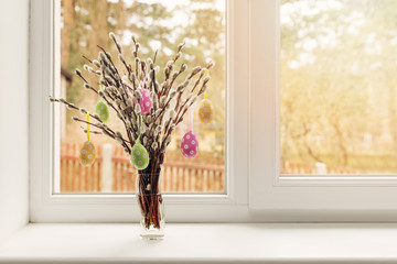 easter decoration - vase with colorful eggs hanging in pussy willow branches on window sill