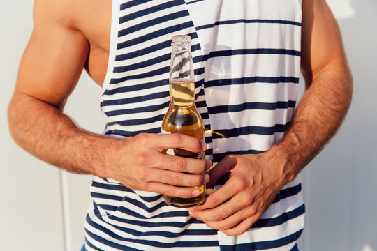 Close-up photo of male hands holding a bottle of beer, outdoors