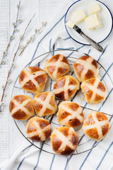 Easter traditional hot cross buns homemade on wooden tray with linen textile and willow branches on white wooden background. Selective focus. Top view. Copy space.
