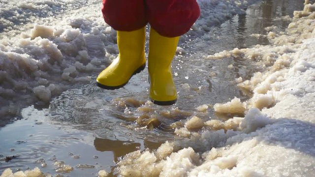 Kid in rainboots jumping in the ice puddle