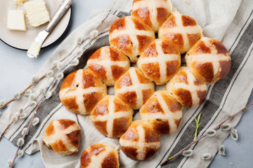 Easter traditional hot cross buns homemade on wooden tray with linen textile and willow branches on old stone or concrete background. Selective focus. Top view. Copy space.
