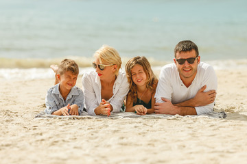 beautiful happy family lying on sandy beach and looking at camera