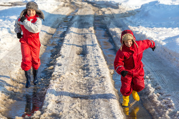 Two kids in rainboots running on the ice puddle