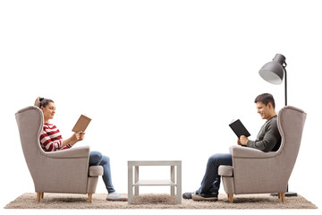 Young man and a young woman seated in armchairs reading books