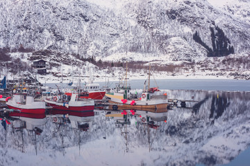 Scenery winter landscape in the Norway. Fishing boats on the mountain ridge background with reflection in the lake in sunset light, Laupstad, Lofoten Islands