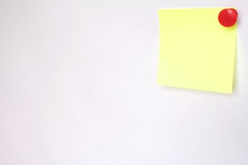 yellow sticker pinned by red button to white wall 1