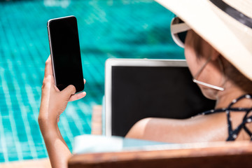 Beautiful Woman working on laptop and mobile smart phone near swimming pool