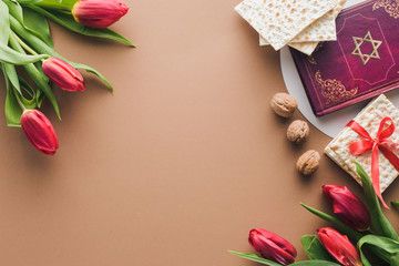 top view of traditional book with text in hebrew, bouquets of red tulips and matza on table