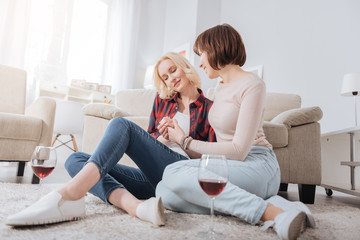 Fototapeta na wymiar Romantic evening. Joyful positive delighted women sitting together and enjoying wine while spending time at home