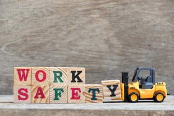 Toy forklift hold letter block Y to complete word work safety on wood background