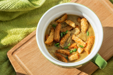 vegetable soup-puree with croutons and green onions in a soup Cup on a wooden Board with a light green towel