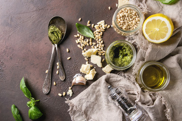 Traditional Basil pesto sauce in glass jar with ingredients above fresh basil, olive oil, parmesan...