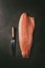 Fotobehang Whole raw uncooked salmon fillet with chef's knife over dark brown texture background. Top view, space. © Natasha Breen