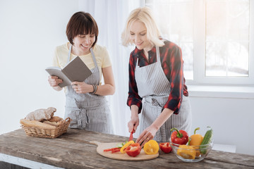 Healthy dish. Happy nice positive woman standing in the kitchen and cutting vegetables while preparing a salad