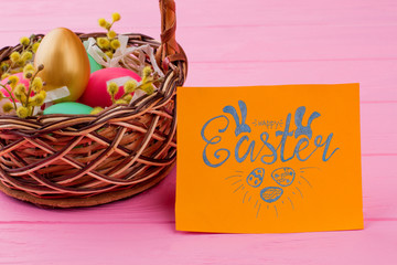 Wicker basket with colorful Easter eggs. Golden egg among colorful Easter eggs in basket. Easter greeting card on pink background.
