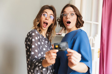 Shocked young women shopaholics showing credit card.