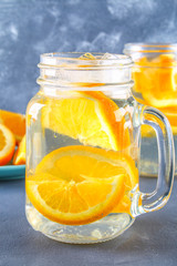 Orange detox water in mason jars on a gray concrete background. Healthy food, drinks.