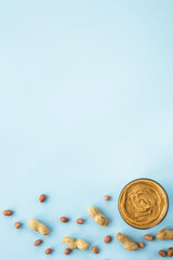 A jar of hazelnut paste among peanuts in shell and without on a blue background. Vegan product. American breakfast. Top view, Flat lay, Copyspace