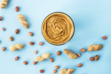 A jar of hazelnut paste among peanuts in shell and without on a blue background. Vegan product. American breakfast. Top view, Flat lay