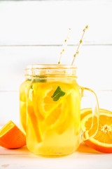 Orange detox water in mason jars on a white wooden table. Healthy food, drinks.
