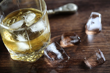 Whiskey in a glass and pieces of ice on a wood