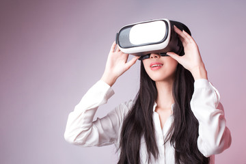 Studio Portrait of young beautiful smiling Asian girl in white shirt watching video in virtual reality headset glasses. Free copy space provided. New technologies concept