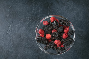Glass plate with ripe red blackberries and raspberries on a black surface.
