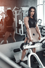 Fototapeta na wymiar Full length portrait of a young attractive sexy beautiful fitness girl in black tank top and shorts standing in gym near training apparatus showing her press and looking at camera. Daria Manyilenkova