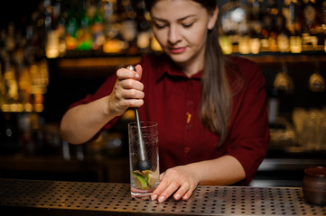 Female bartender pressing down a cane sugar with lime in a glass