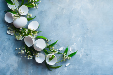 Header with raw eggs, decorative green leaves and spring flowers. Modern Easter concept with copy space. High key concrete background.