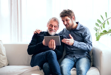 Hipster son and his senior father with tablet at home.