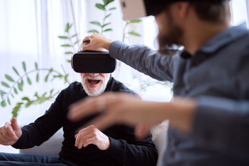 Hipster son and his senior father with VR goggles at home.