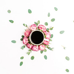 Cup of coffee in frame of pink rose flower buds and eucalyptus branches on white background. Flat lay, top view.