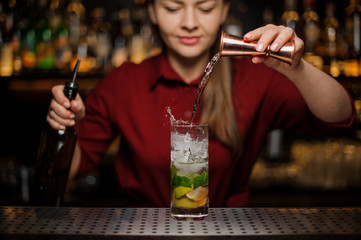 Female bartender pouring out a transparent drink from the measuring pile with splash
