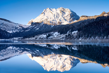 Wägitalersee mit Spiegelung des schneebedeckten Fluebrig, Eisschicht, Winterlandschaft, Bergwald, Schatten, Sonne, blauer Himmel
